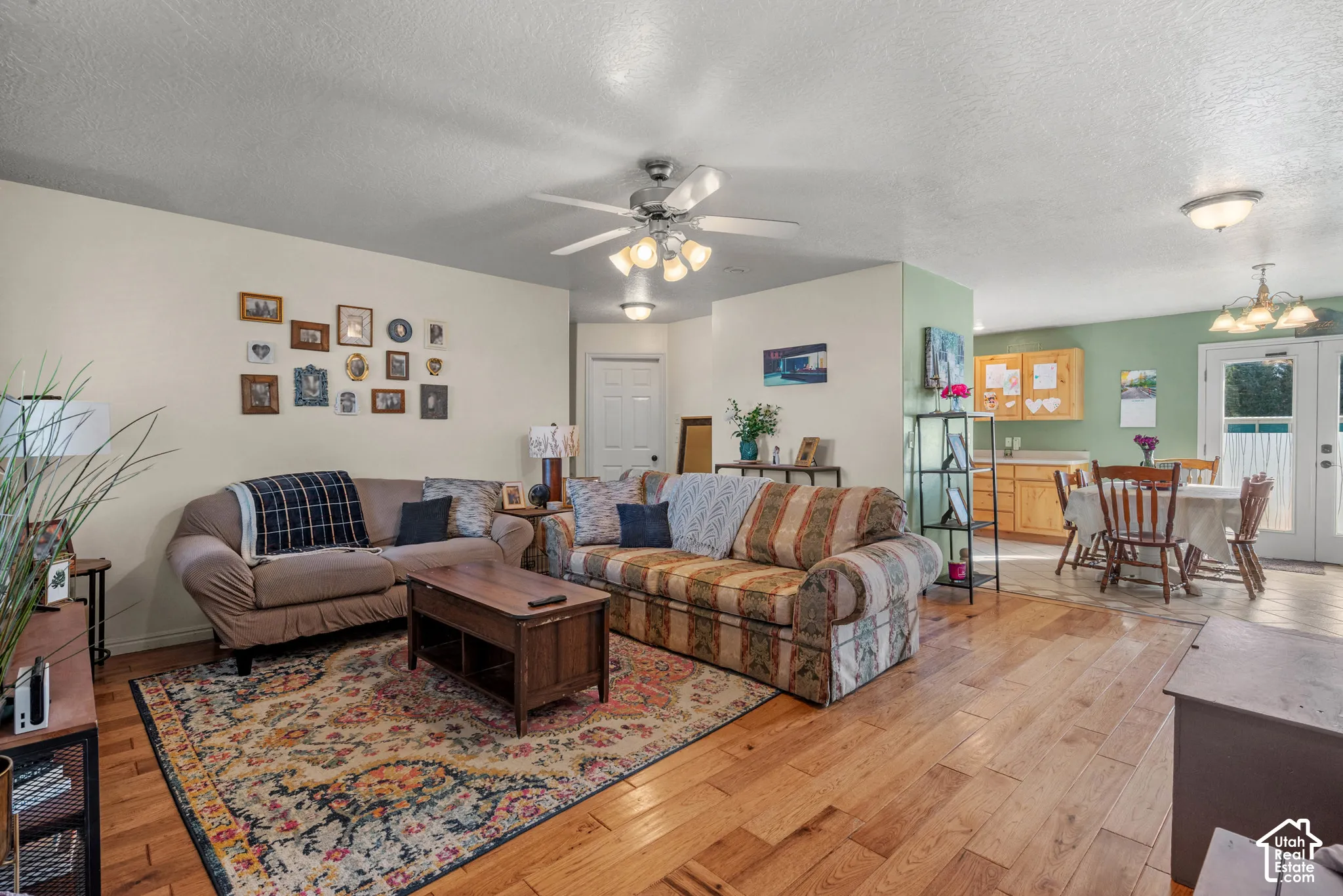 Wood-finish flooring throughout, ceiling fan with light fixture, recessed lighting, and kitchen area with wood cabinetry and French doors