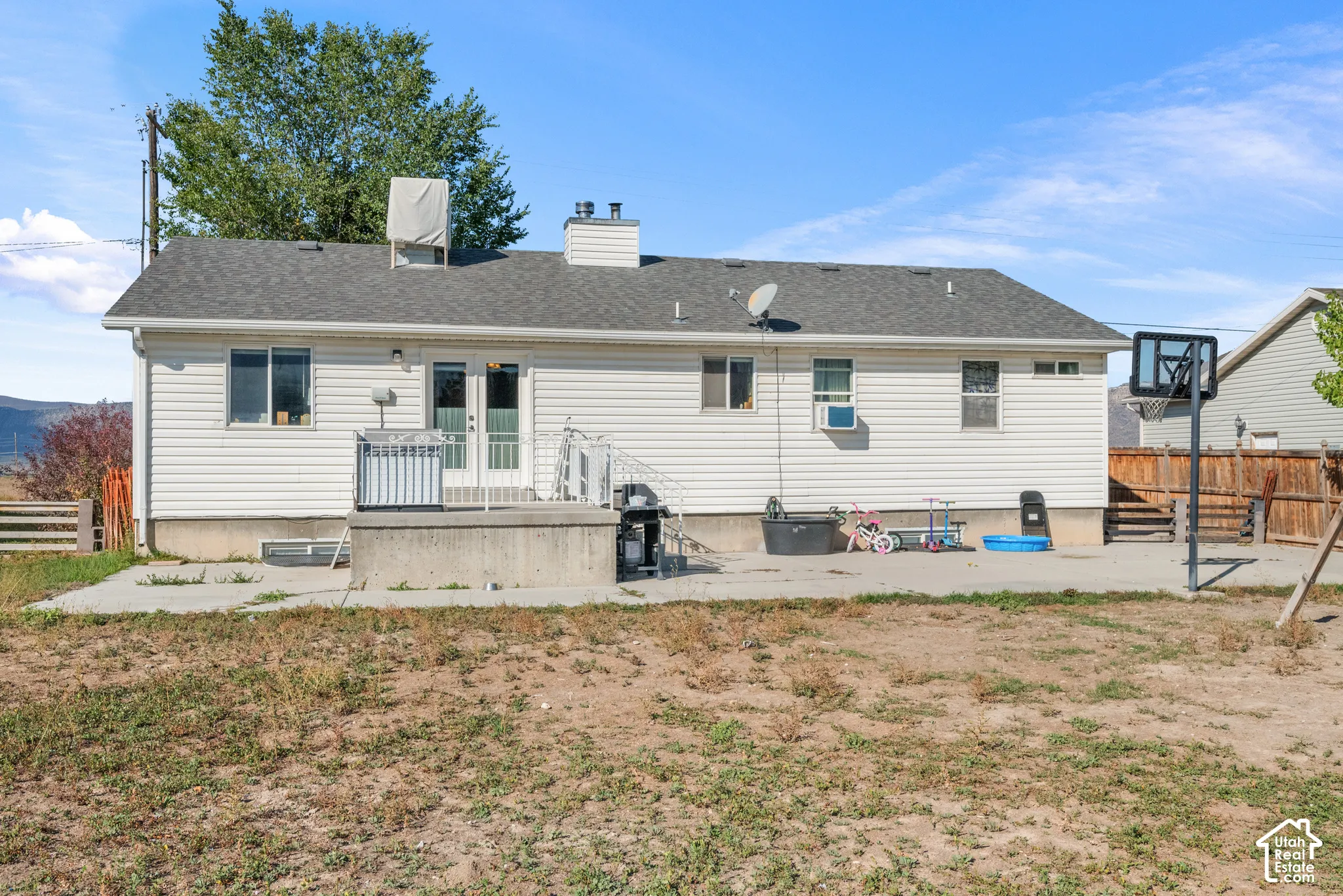 Rear exterior with white siding, a concrete patio, and a grey shingle roof