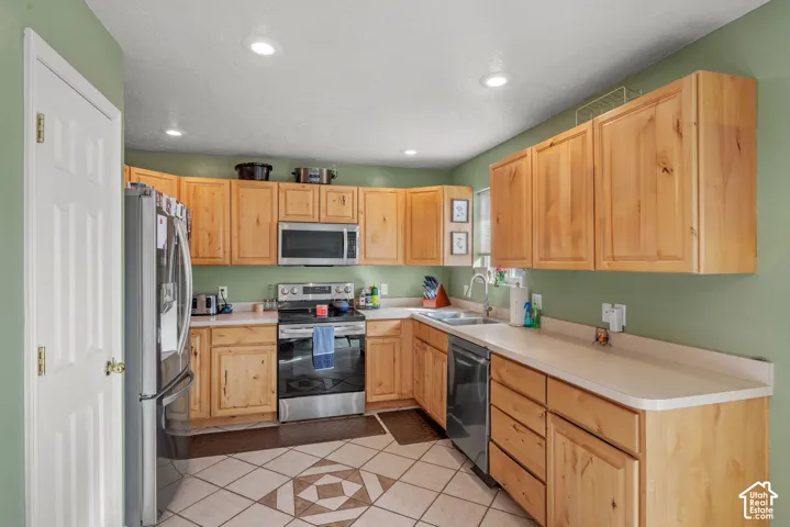 Well-appointed kitchen featuring light wood cabinetry, light-toned countertops, tile flooring with geometric patterns, recessed lighting, and stainless steel appliances