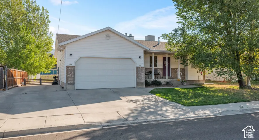 White siding exterior with a two-car garage, covered porch entry, partial stone facade, and concrete driveway