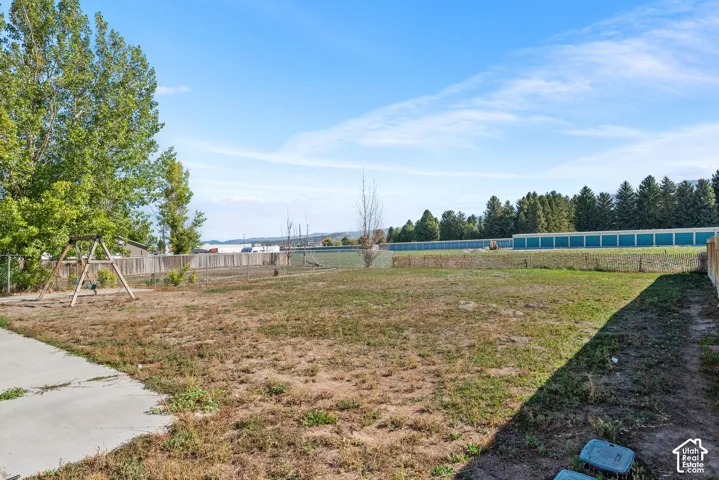Expansive grassy yard with a concrete patio, mature trees, and wood fencing