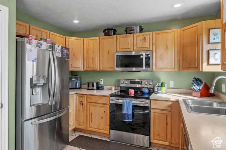 Corner kitchen featuring wood-finish cabinetry, stainless steel appliances, recessed ceiling lighting, and a double basin sink