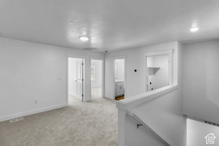 Carpeted landing with white walls, recessed lighting, and a white stair railing