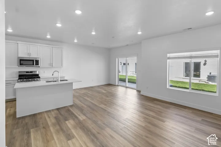 Open-concept living area featuring wood-finish flooring, white cabinetry, stainless steel appliances, and a kitchen island with an integrated sink