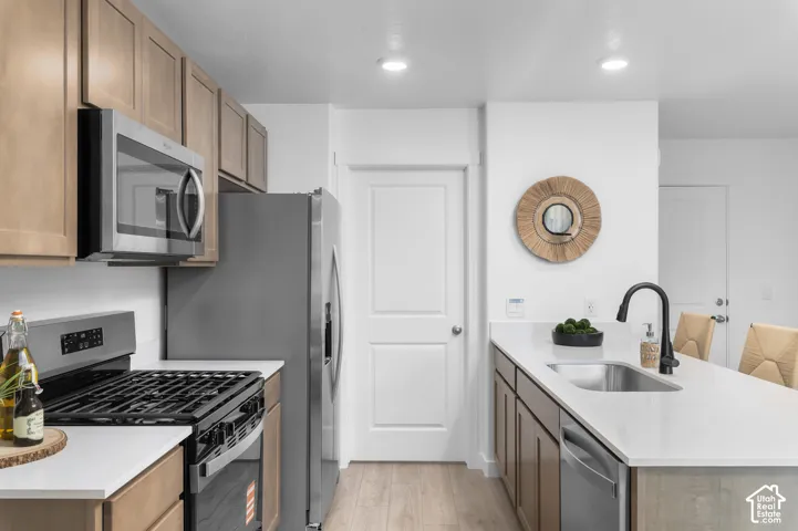 Kitchen featuring stainless steel appliances, light wood-finish cabinetry, white countertops, and a stainless steel sink with a black faucet