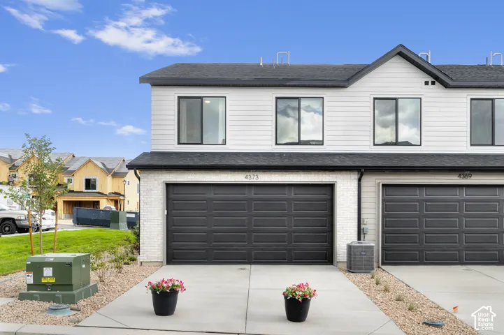 Modern townhome exterior featuring light-colored siding, dark-frame windows, and a dark asphalt shingle roof