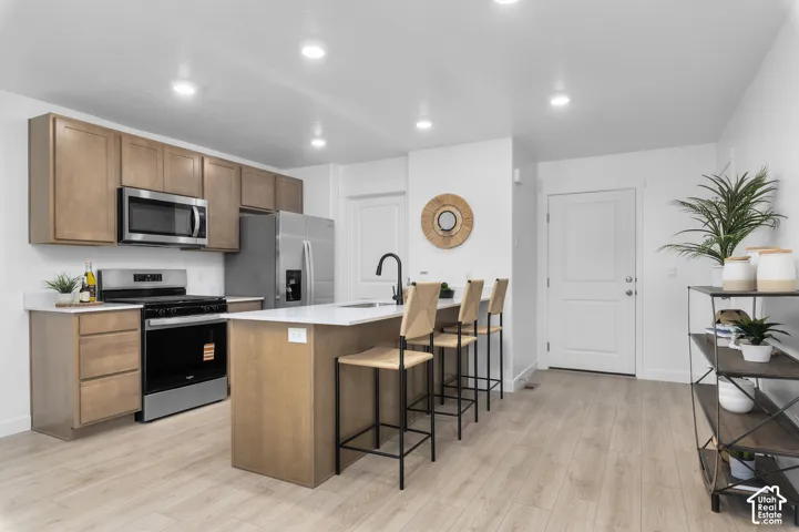 Kitchen featuring wood-finish cabinetry, stainless steel appliances, a center island with seating, and light wood-finish flooring