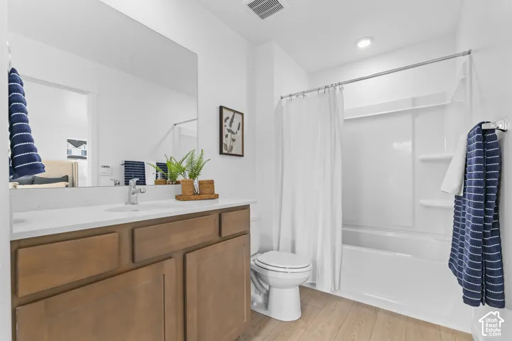 Bathroom featuring a single vanity with wood-finish cabinetry, a large wall-mounted mirror, a white countertop, and a white tub with shower