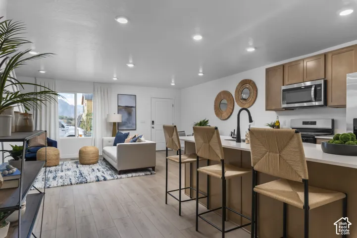 Kitchen island with counter seating, stainless steel appliances, wood-finish flooring, recessed lighting, and large windows