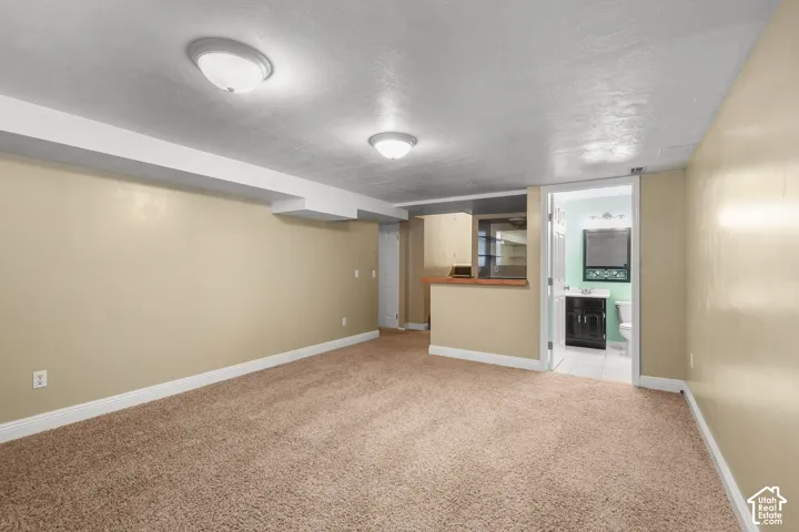 Expansive carpeted area with recessed lighting, integrated bar counter, and an adjacent bathroom featuring a vanity with sink