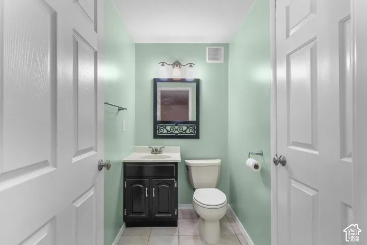 Recessed lighting, wood-finish vanity with countertop, wall-mounted mirror, and tile flooring