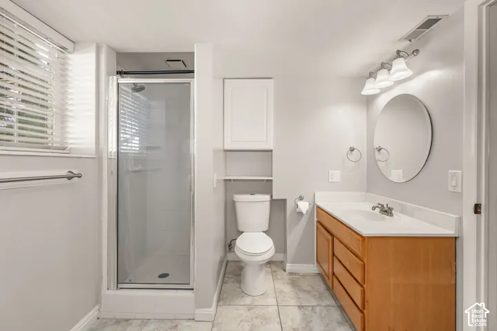 Tiled flooring, glass-enclosed shower, wood-finish vanity with an integrated sink, wall-mounted light fixture, and oval mirror