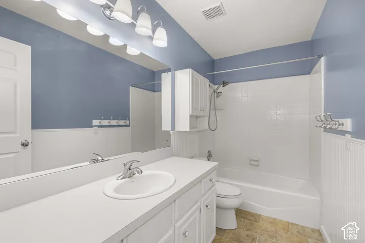 White paneled wainscoting, a chrome fixture vanity light, an integrated sink with a chrome faucet, a white tiled tub surround, and a coordinating vanity cabinet