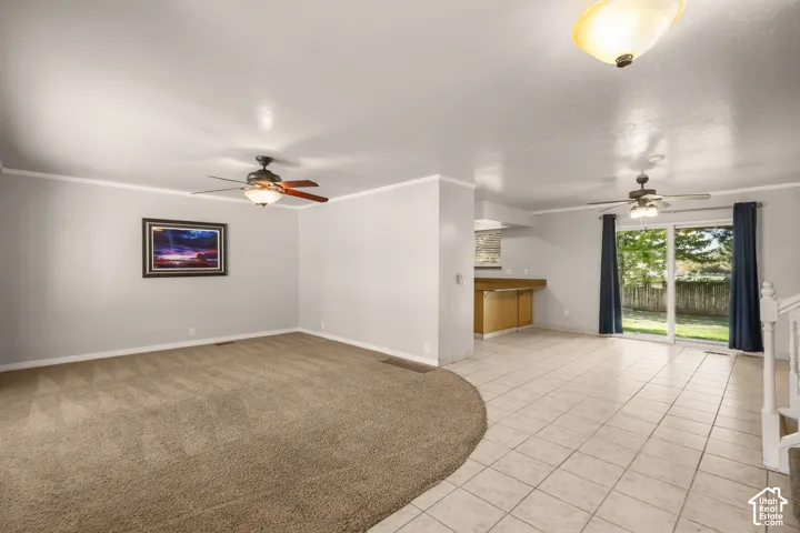 Spacious open-concept room featuring a ceiling fan, sliding glass doors, built-in cabinetry with a countertop, and a mix of carpet and tile flooring