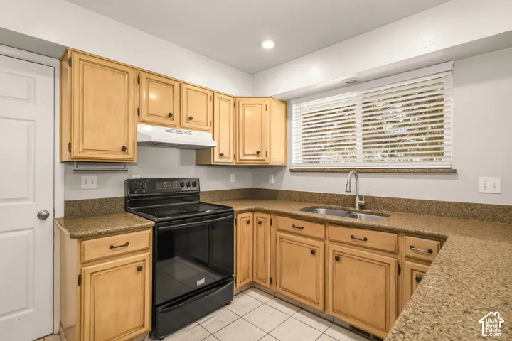 Kitchen featuring light wood-finish cabinetry, speckled countertops, a double basin sink with a chrome faucet, a black range, and white tiled flooring