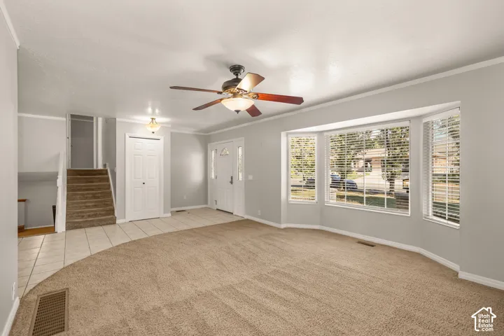 Bay window with blinds, ceiling fan, carpet and tile flooring, and a front entry door with side lites