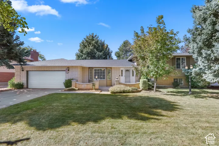 Brick exterior with an attached garage, mature landscaping, and a paved driveway
