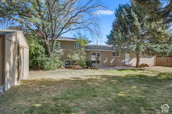 Expansive backyard featuring a storage shed, established trees, and a ground-level patio