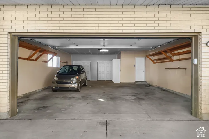 Attached garage with concrete flooring, overhead wooden shelving, and interior access doors