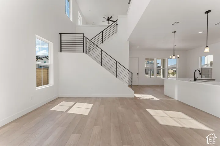 High ceilings, wood-finish flooring, contemporary staircase with black metal railings, white kitchen island with sink and faucet, and multiple windows providing ambient light