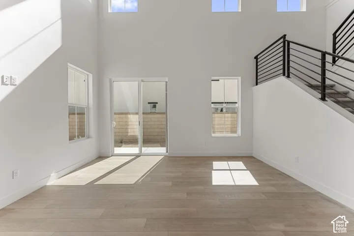 Vaulted ceilings with high windows, wood-finish flooring, sliding glass door, and modern black metal stair railing