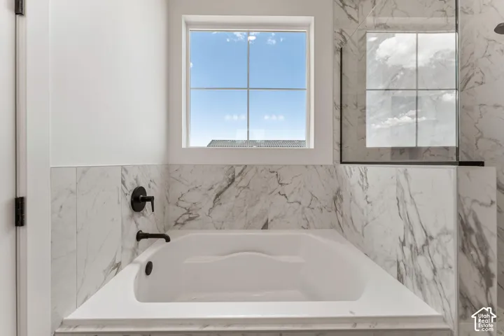 Built-in soaking tub with matte black fixtures, surrounded by white marble-look tiling, and a large window with grid panes