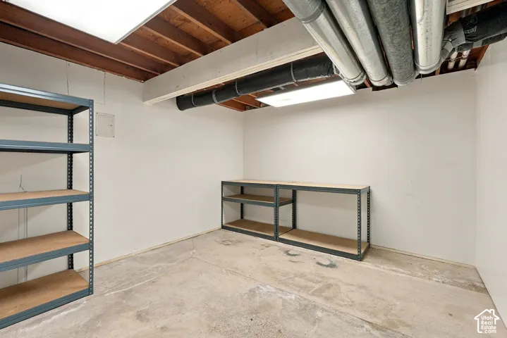Utility room with exposed ceiling joists, concrete flooring, and overhead fluorescent lighting