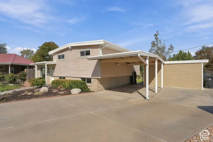 Beige siding exterior with a concrete driveway, attached carport, detached garage, and a landscaped front yard with decorative rocks