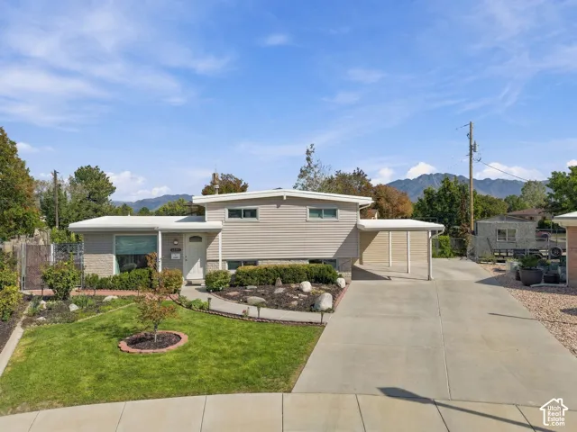 Split-level residence featuring a carport, concrete driveway, and a front lawn with established landscaping