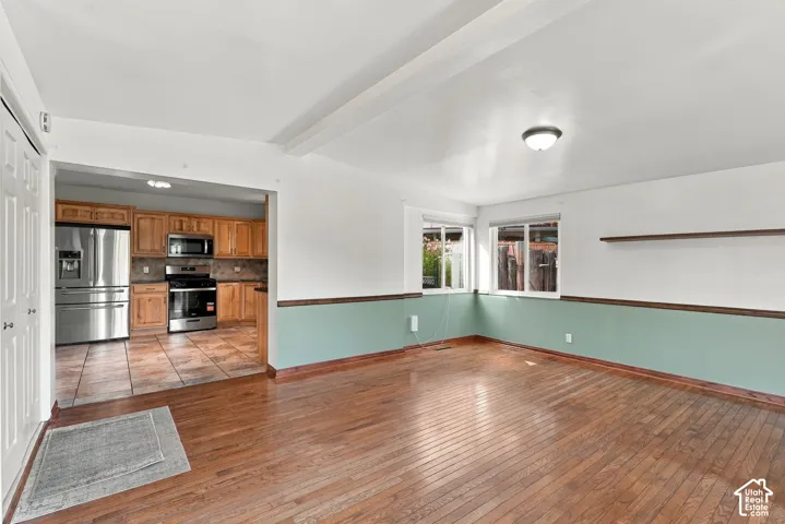 Hardwood flooring in living area, two windows providing natural light, kitchen with stainless steel appliances, wood cabinetry, and tile flooring