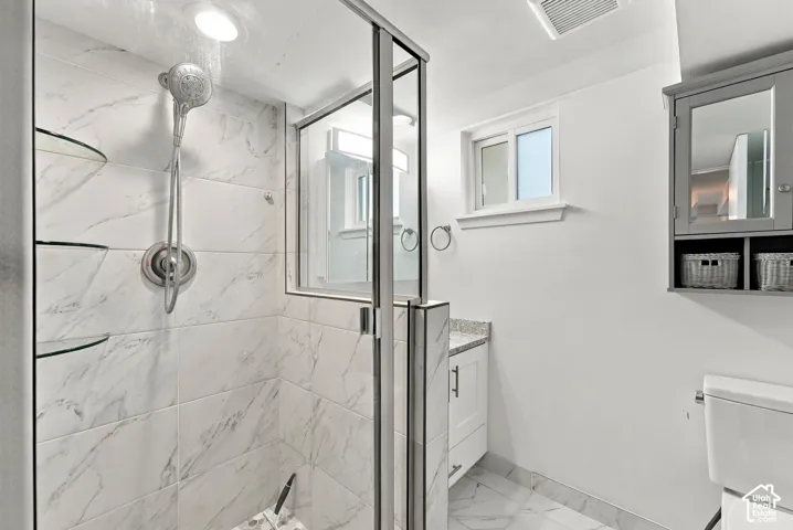 Shower with white marble-look tile, glass shelving, and a handheld showerhead