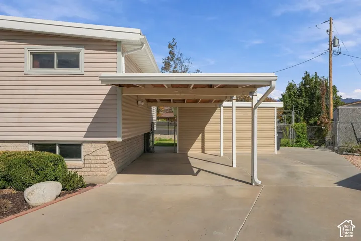 Carport with concrete driveway, light beige horizontal siding, and light brick foundation