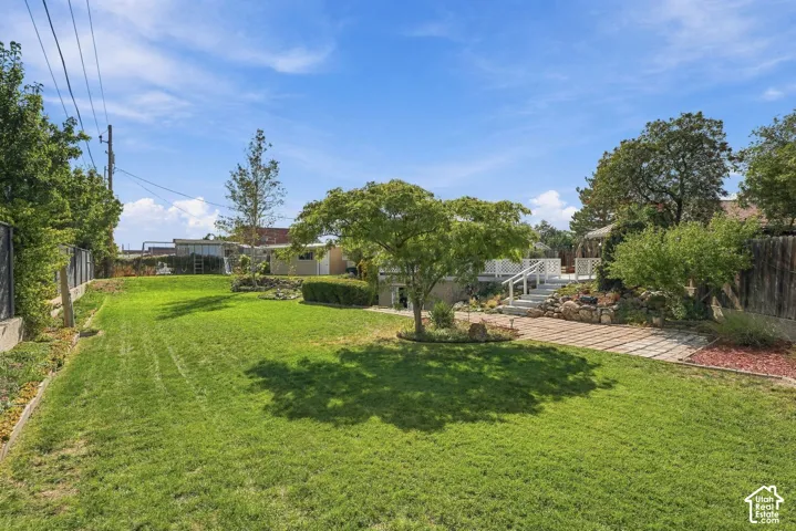 Expansive backyard featuring a manicured lawn, established trees, a multi-level deck with white railings, and a stone retaining wall