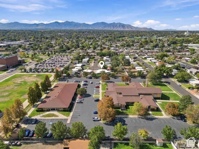 Expansive property featuring two distinct structures, multiple paved parking areas, and mature landscaping, all set against a backdrop of distant mountains