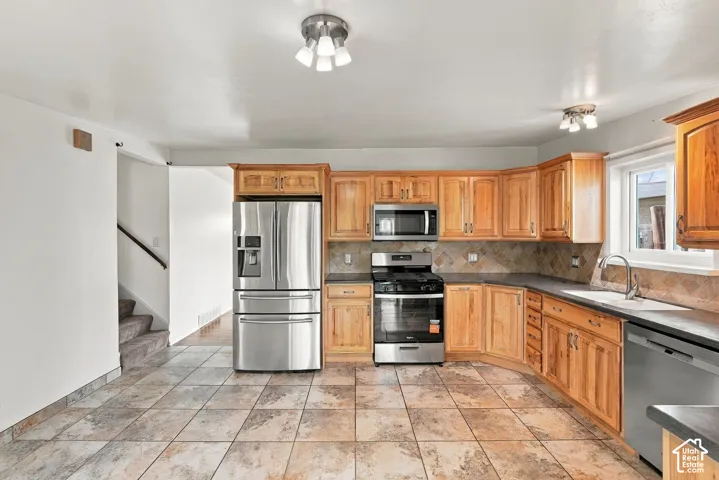 Kitchen featuring stainless steel appliances, wood cabinetry, tile flooring, and a tile backsplash