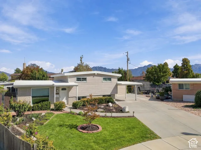 Split-level residence featuring brick and siding exterior, a front yard with manicured lawn, established landscaping, and a paved driveway with an attached carport