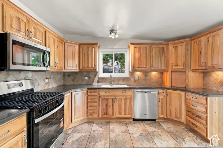 Kitchen featuring light wood cabinetry, dark countertops, a tile backsplash, and stainless steel appliances