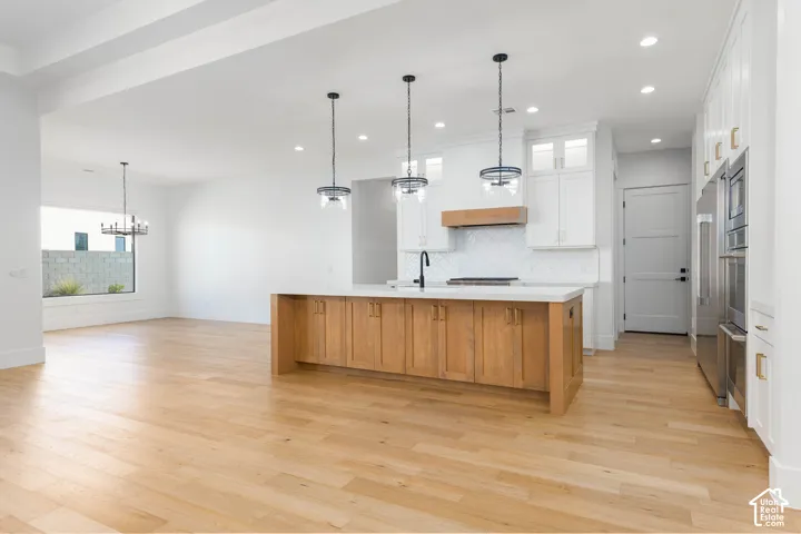 Open-concept kitchen and dining area featuring a wood-finish island with substantial base cabinetry, white cabinetry, stainless steel appliances, pendant lighting, and wide-plank wood-finish flooring throughout