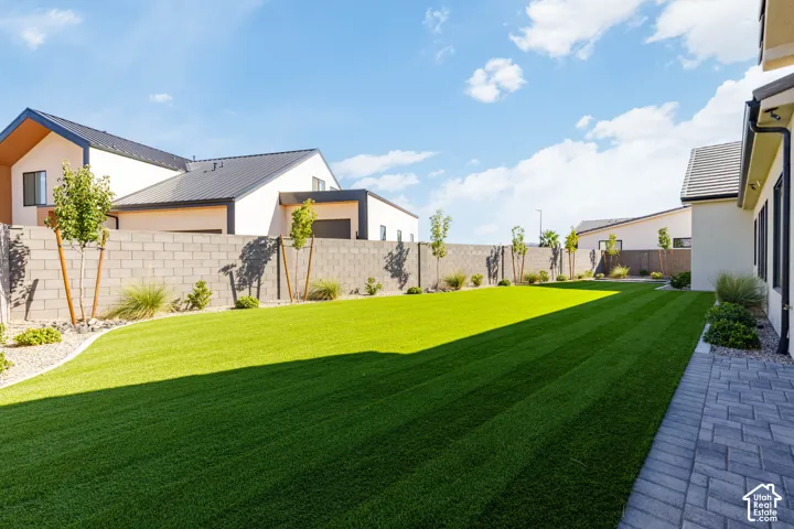 Expansive backyard featuring artificial turf, a paver patio, a perimeter block wall, and mature landscaping