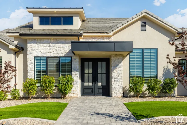 Stucco exterior with stone accents, a tile roof, and a paver walkway leading to a double entry door with glass panels
