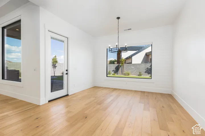 Bright, open room featuring warm wood-finish flooring, white walls, and abundant natural light from dual glass doors and large framed window