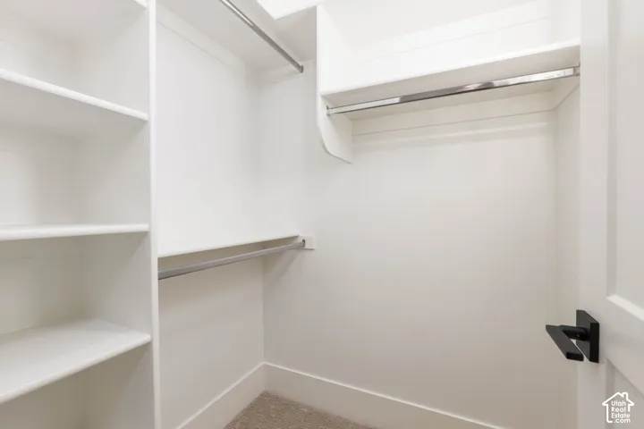Built-in closet system featuring white shelving, multiple hanging rods, and carpet flooring