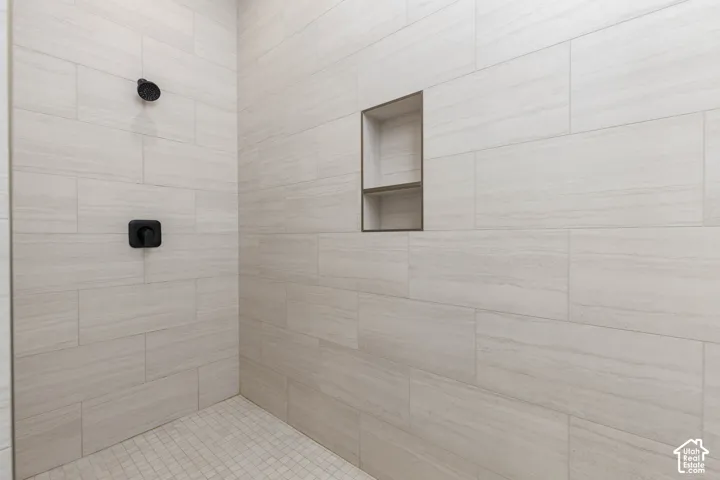 Subway tile shower surround with a matte black shower head and control, featuring a built-in shower niche and mosaic tile flooring
