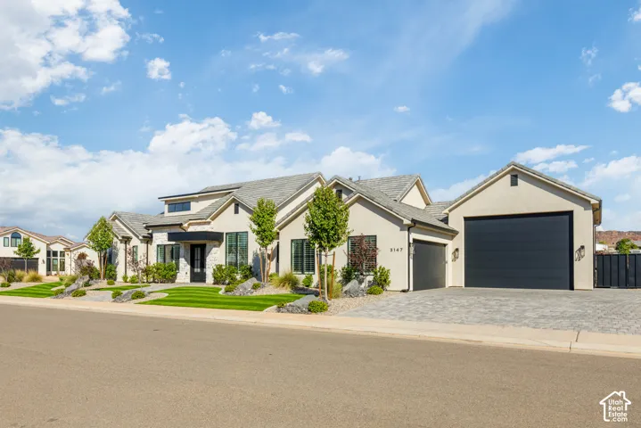 Stucco exterior with stone accents, a multi-car garage, paver driveway, and manicured landscaping