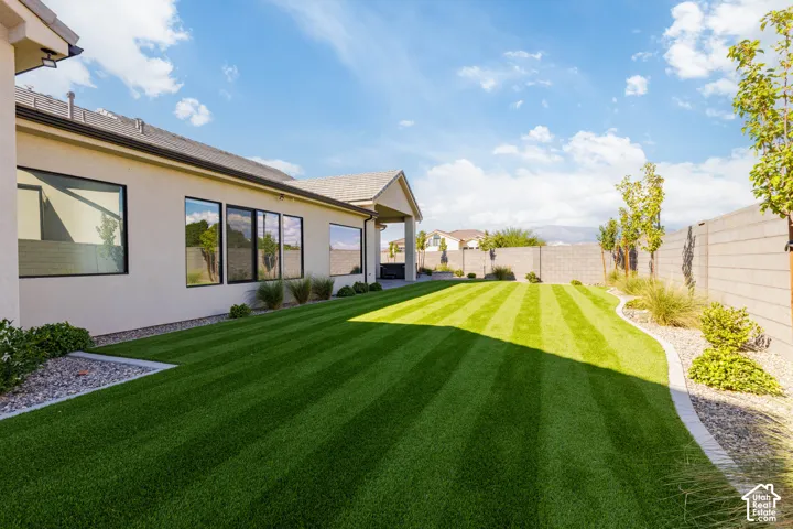 Expansive backyard featuring professionally manicured lawn with precision striping, mature landscaping along perimeter fencing, decorative gravel accents, and modern architectural siding with multi-panel glass doors opening directly to outdoor living spac