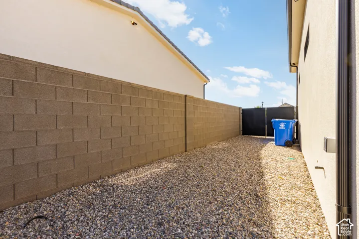 Gravel side yard with a block wall, black metal gate, and exterior stucco finish
