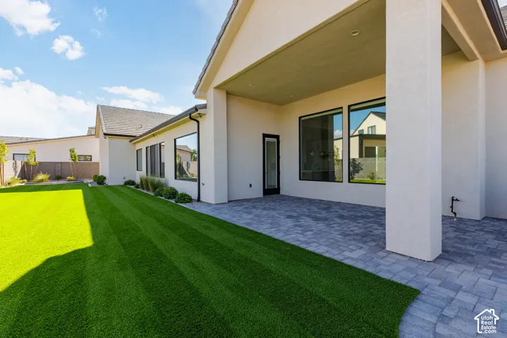 Expansive backyard featuring a manicured artificial lawn, a paver patio, and covered outdoor living space