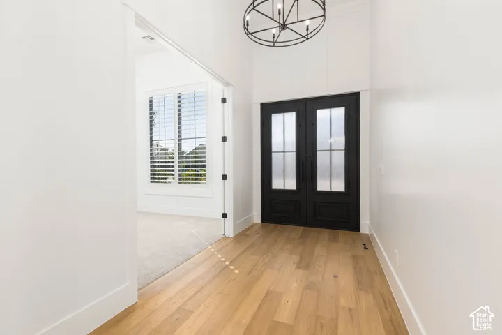 Double entry doors with glass panels, wood-finish flooring, a contemporary chandelier, and a room with plantation shutters