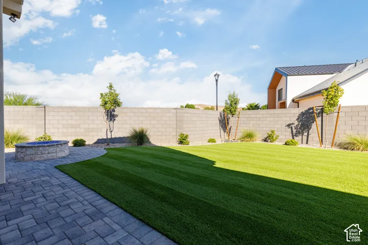 Expansive backyard featuring a paver patio, a stone-clad fire pit, a manicured lawn, and perimeter landscaping