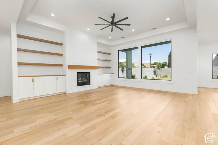 Spacious living area featuring light wood-finish flooring, a white brick fireplace with a wood mantel, and built-in shelving with cabinetry